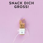 Oben steht "Snack dich groß!" in schwarzer Schrift. Ein Müsliriegel, verziert mit einem Lächeln auf Papier.