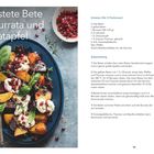 "Geröstete Bete mit Burrata und Granatapfel." Ein Teller mit buntem, geschichtetem Gemüse, Burrata, Granatapfelkernen und Kräutern.