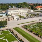 Ein elegantes, historisches Gebäude umgeben von kunstvoll gestalteten Gärten mit symmetrischen, grünen Mustern.