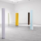 Texte: "Exhibition view Anne Truitt: Sculpture, 1962-2004". Mehrere bunte, schlanke Säulen stehen in einem weißen Raum.
