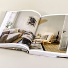 Offenes Buch, zeigt ein stilvoll eingerichtetes Wohnzimmer mit Sofa, Sessel und Holzboden. Neutral gehaltene Farben.