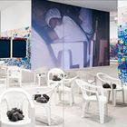 „CUBA ES“ auf bunter Graffiti-Wand, weiße Plastikstühle mit dunklen Objekten in modernem Raum.