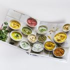 Ein aufgeschlagenes Buch zeigt verschiedene bunte Dips in Schüsseln auf einer Kachelfläche, dekoriert mit Kräutern.
