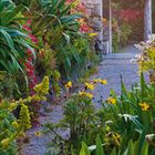 Kalenderseite Juli 2027: Eine malerische Gartenszene mit Pflanzen, Sonnenstrahlen und einem Pavillon mit rotem Ziegeldach.