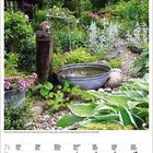 Kalenderseite für Juli 2022. Ein idyllischer Garten mit Wasserschale, blühenden Pflanzen und einem alten Wasserhahn.