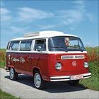 "California Style" steht auf einem retro roten VW-Bus auf einer ländlichen Straße, umgeben von grüner Natur.