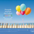 „Freunde machen das Leben bunter.“ Bunte Luftballons am Strand über einem Holzzaun. Unten Kalender für Juli.
