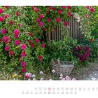 "Juli" in fließender Schrift. Kalender für 2022. Üppige Rosen an einem Holzzaun, Strohhut, Weidenkorb, blühende Pflanzen.