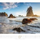Kalender für Juli; Foto vom Meer mit großen Felsen und Bäumen im Hintergrund, klare Wellen am Strand.