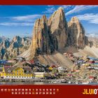 Kalenderseite mit Monat Juli, rot-gelbem Design. Farbige Häuser vor majestätischen Felsen in einer bergigen Landschaft.