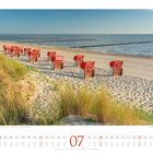 Kalenderblatt Juli. Strandkörbe in Reihen am Sandstrand, Meer im Hintergrund, Gräser im Vordergrund.