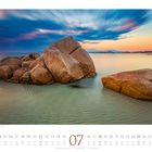 Kalenderseite Juli, Strandansicht mit Felsen in klarem Wasser bei Sonnenuntergang, lebendige Farben mit sanften Wellen.
