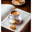 06 FEBRUAR. Eine Tasse Espresso und Kekse auf einem offenen Buch, daneben eine Schale Kekse.