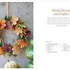 "Blätterkranz aus Papier" und Anleitung. Ein Kranz aus buntem, gefaltetem Papier in Herbsttönen an einer Wand.