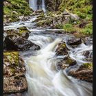 Kalenderblatt mit Juli-Kalender und Wasserfall zwischen felsigen Klippen. Fließender Fluss mit moosbewachsenen Steinen.