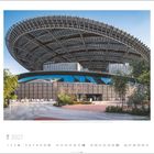 Text: "MUDRA", "7", "2027". Moderne Struktur mit riesigem, geschwungenem Dach; Garten im Vordergrund.