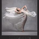 Juli | July. Elegant tanzende Frau in fließendem, weißem Kleid vor grauem Hintergrund. Kalenderdarstellung für Juli.