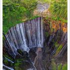 Kalender, Monat Juli. Landschaft mit Wasserfall, üppigem Grün und einem fernen, bläulichen Berg unter blauem Himmel.