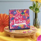 „Lebe das Leben. Farbenfrohe Inspirationen voller Lebenslust.“ Ein Tischkalender mit bunten Blumenmotiven, daneben Blumen.