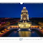 Völkerschlachtdenkmal Leipzig. Eine beleuchtete Struktur bei Nacht, mit einem Wasserbecken davor. Ein Kalenderblatt für Juli.
