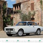 Kalender für Juli, zeigt einen weißen Alfa Romeo GT 1300 Junior Baujahr 1972 in einer malerischen Altstadtstraße.