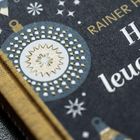 Text: "Rainer", "Hell leuchter St". Goldenes Muster mit Ornamenten und weißen Punkten auf dunklem Hintergrund.