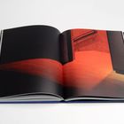 Ein aufgeschlagenes Buch zeigt eine Fotografie mit intensiv rot-orangem Licht auf einer Treppe.
