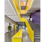 Erweiterung Grund- und Mittelschule, München. Innenbereich mit gelben und violetten Akzenten, Treppe, Personen, moderner Stil.