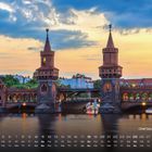 „Oberbaum Brücke“ und Kalenderdaten unten. Malerische Brücke mit Türmen über ruhigem Wasser bei Sonnenuntergang.