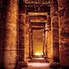 Massive Steinsäulen in einer antiken, schmal beleuchteten ägyptischen Tempelhalle, komplizierte Hieroglyphen sind eingraviert.