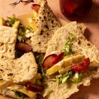 Fladenbrot gefüllt mit Salat, gelber Paprika und roten Pflaumen. Daneben ein Glas mit roten eingelegten Zutaten.