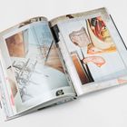 Ein Buch zeigt technische Zeichnungen und Skulpturen. Links sind Spiralförmige Drähte, rechts rötliche Anatomiemodelle.