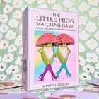 Text: „THE LITTLE FROG MATCHING GAME“. Illustration: Zwei Frösche in High Heels, mit Fliegenpilz-Hüten, auf pastellfarbenem Hintergrund.