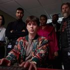 Sechs Personen in einem Büro; eine Person im Vordergrund tippt. Verschiedene Ausdrucke von Aufmerksamkeit und Nachdenklichkeit.