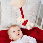 Ein Baby schaut auf ein Plüschspielzeug in Form eines Bären, das über ihm hängt. Es liegt auf einer roten Decke.