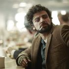 Ein Mann mit lockigem Haar und Bart sitzt in einem Café. Er trägt eine braune Cordjacke und raucht eine Zigarette.