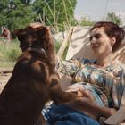 Eine Frau liegt in einem Liegestuhl, streichelt einen Hund und hält ihren Babybauch. Im Hintergrund ein Mann im Garten.