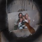 Ein Familienfoto mit vier Personen ist an eine bemalte Wand gepinnt, ein Griff steckt im Bild.