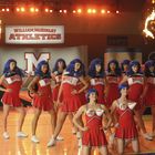 „William McKinley Athletics“, Cheerleader in roten Uniformen, blaue Perücken, Feuerjongleure im Hintergrund.
