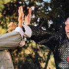 Zwei Männer in traditioneller Kleidung kämpfen mit Händen im Freien. Der eine trägt eine rote Schärpe um den Hals.