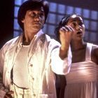 Zwei Personen in heller Kleidung schauen konzentriert. Eine hebt die Faust, die Szene wirkt dynamisch und dramatisch.