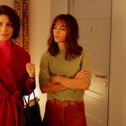 Text: "VOGUE", "Nueva Actitud". Zwei Frauen in einem Raum; eine in rotem Mantel, die andere in grünem Pullover. Ein Bücherregal.