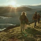 Eine Gruppe von Menschen wandert einen grasbewachsenen Hügel hinunter Richtung Gletscher bei Sonnenuntergang.
