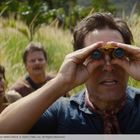 Drei Personen stehen in hohem Gras. Eine Person vorne schaut durch ein Fernglas, zwei andere blicken interessiert.