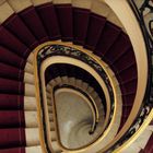 Eine Frau steigt eine Wendeltreppe mit rotem Teppich und verziertem Geländer hinauf.