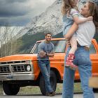 "FORD"-Schriftzug auf einem orangefarbenen Pickup. Ein Mann lehnt lächelnd daran. Eine Frau hält ein Kind auf dem Arm. Hintergrund: Berge.