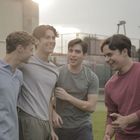 Vier junge Männer lachen und umarmen sich auf einem Sportplatz im Freien.