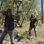 Zwei Männer im Wald zielen mit Bögen, einer mit einem modernen Compoundbogen, der andere mit einem traditionellen Bogen.