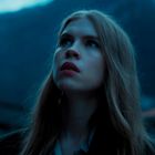 Eine Frau mit langen Haaren schaut in einer abendlichen Berglandschaft nach oben.