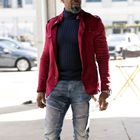 Ich kann den Text nicht erkennen. Ein Mann trägt eine rote Jacke, dunklen Pullover, Jeans und eine Schiebermütze.